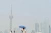Прохожий в Шанхае держит зонт, чтобы защититься от солнца.